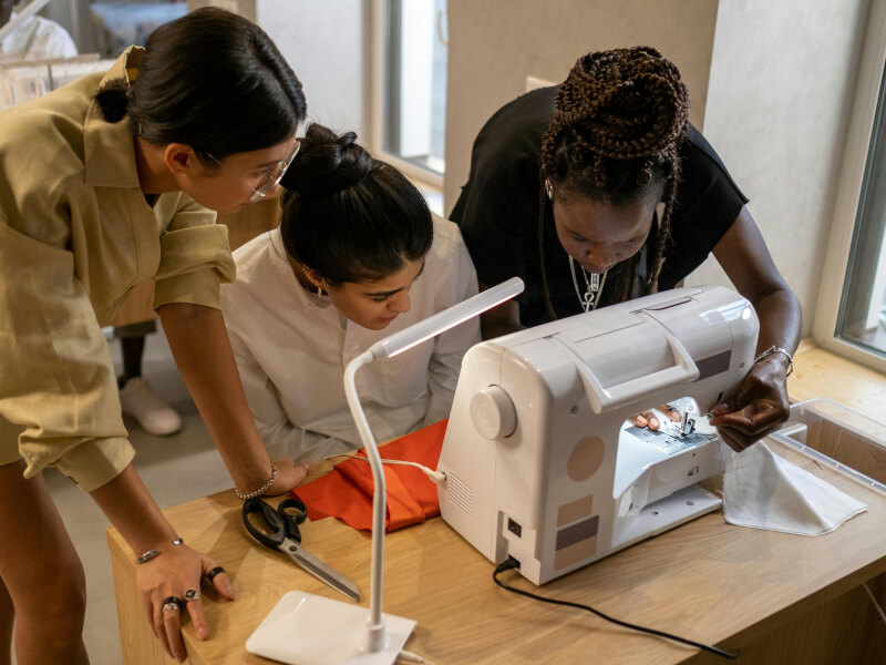 Three young women gathered around a sewing machine